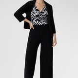 The Puzzle Jumpsuit transitions seamlessly from workwear to evening outings, making it the ultimate wardrobe multitasker Size 10 woman wears her black and white playsuit with Merit Blazer in Black 