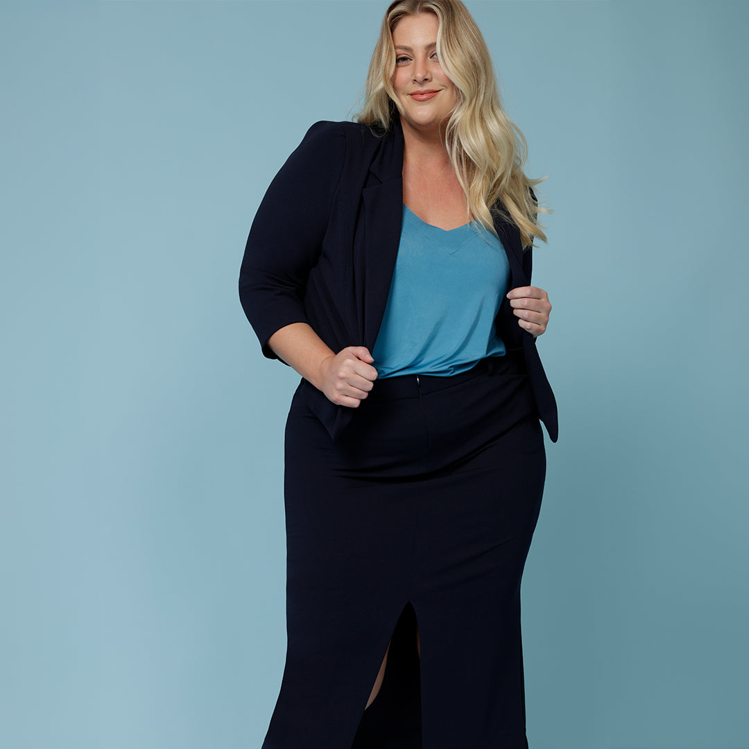 A good blue business suit for women, a curvy woman shows how good this work suit looks as a workwear suit for plus size women. The 3/4 sleeve navy jacket is worn over a blue summer top for women and paired with a straight, navy blue midi skirt to create a skirt suit.