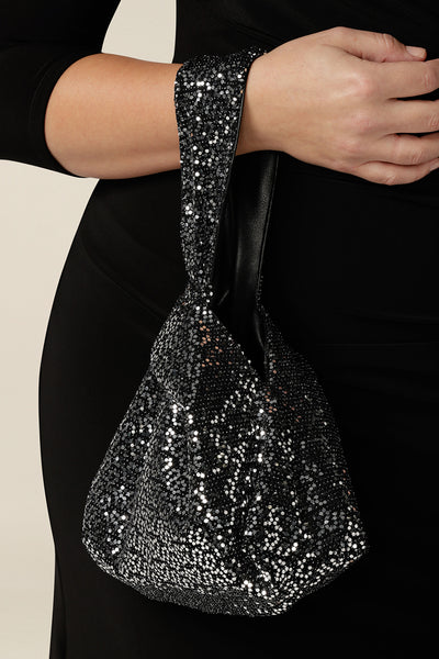 A silver sequin reversible knot bag for evening and event wear. This sparkly evening bag has a black leatherette lining that can be turned inside out as a leather-look black bag for cocktail wear. Made in Australia by women's occasionwear brand, Leina & Fleur.