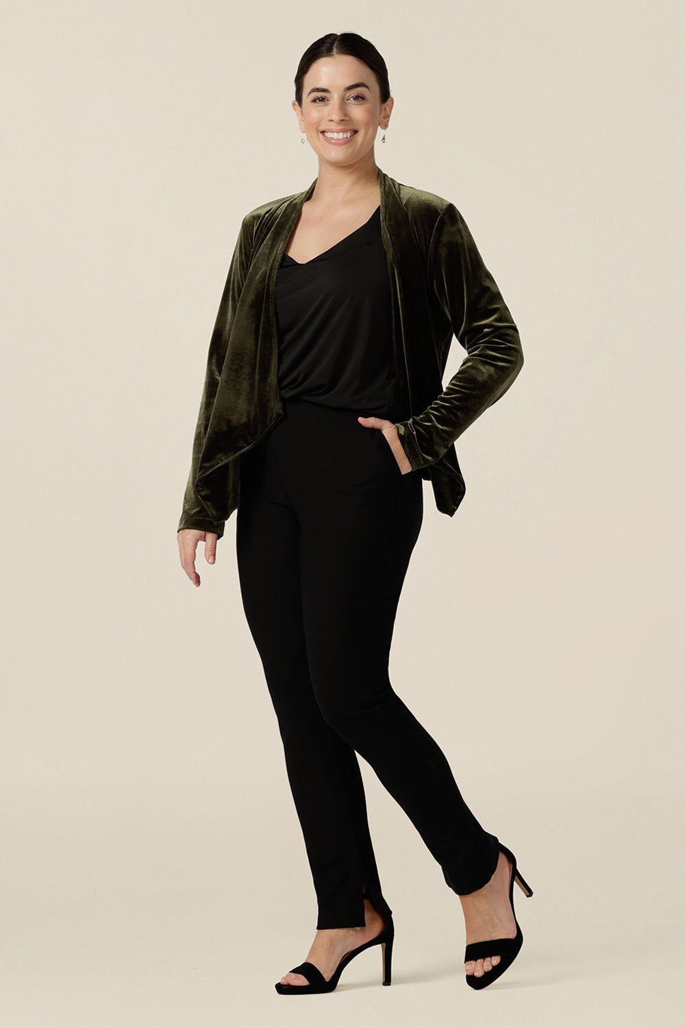 A size 10, petite height woman wears a waterfall front velour jacket for evening and cocktail wear. In bracken green this cocktail jacket worn with a black cami top and black slim leg trousers. A good jacket for evening and wedding guest outfits, step out in style at your next event in made-in-Australian occasionwear by Leina & Fleur.