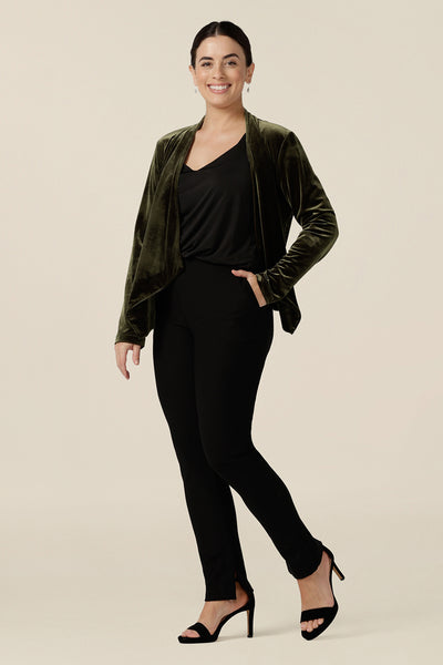 A size 10, petite height woman wears a waterfall front velour jacket for evening and cocktail wear. In bracken green this cocktail jacket worn with a black cami top and black slim leg trousers. A good jacket for evening and wedding guest outfits, step out in style at your next event in made-in-Australian occasionwear by Leina & Fleur.