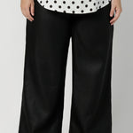 Close up image of black workwear pants, crafted from 100% linen, the fabric has a subtle luxurious sheen and no stretch, enhancing its refined, chic look.