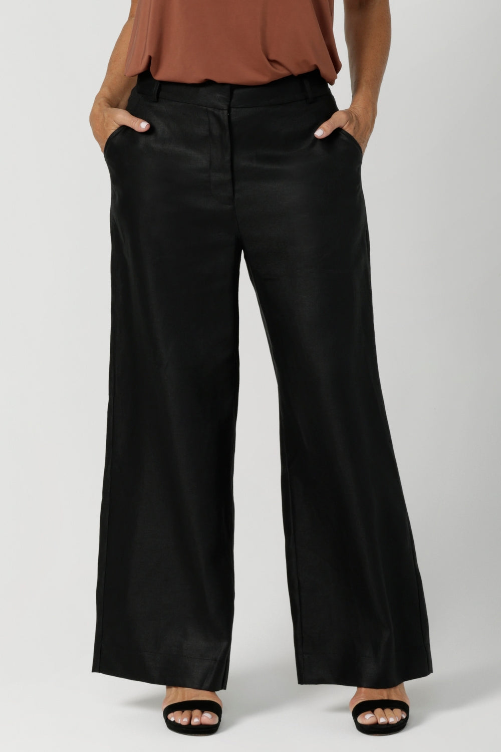 Woman's linen pants are showcased on size 12 woman styled with clay coloured cami & black high heels. This high-rise pant features a functioning waistband with a fly fastening and hook-and-bar closure, complemented by belt loops for added versatility.