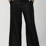 Woman's linen pants are showcased on size 12 woman styled with clay coloured cami & black high heels. This high-rise pant features a functioning waistband with a fly fastening and hook-and-bar closure, complemented by belt loops for added versatility.