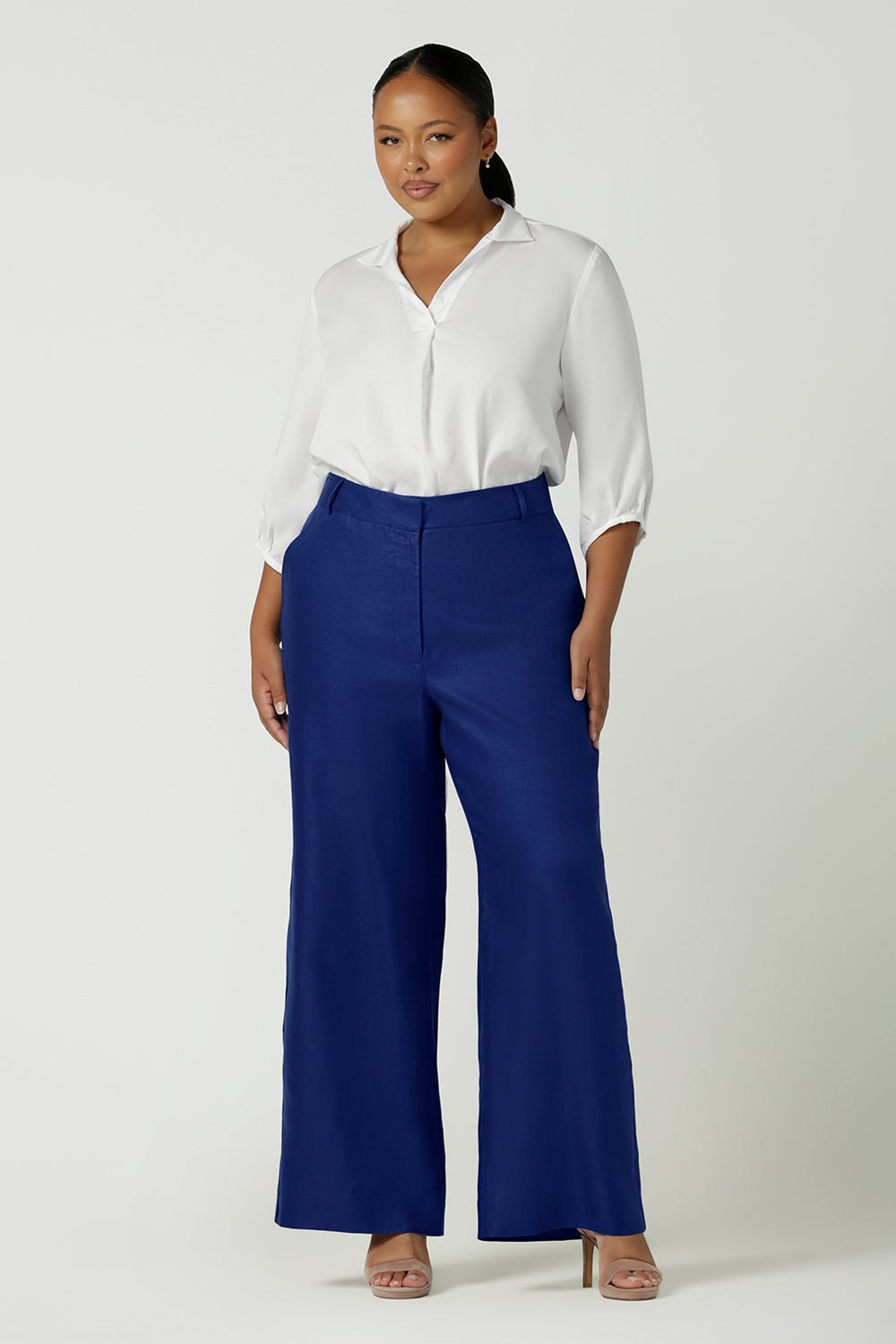 Woman wears a size 16 Ronnie Pant in Cobalt Linen. A high waisted pant in cobalt with a zip fly front, pocket detail and belt loops. Styled back with an Arley Shirt in White. Made in Australia for women size 8 - 24.