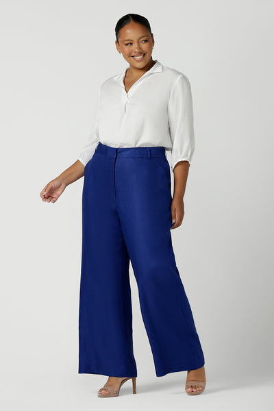 Woman wears a size 16 Ronnie Pant in Cobalt Linen. A high waisted pant in cobalt with a zip fly front, pocket detail and belt loops. Styled back with an Arley Shirt in White. Made in Australia for women size 8 - 24.