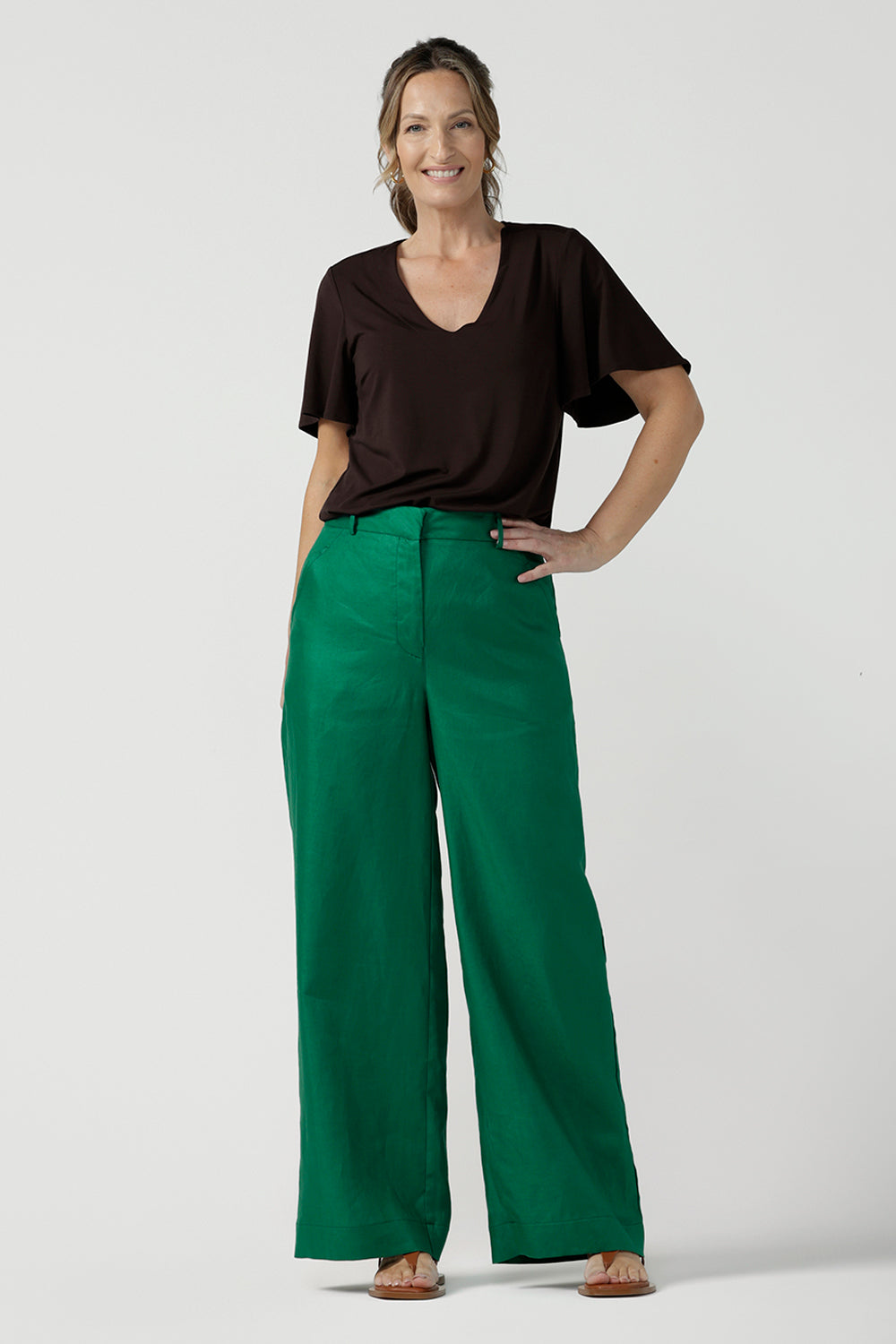 A size 12 woman wears a tailored linen pant in 100% linen. Breathable linen fabrication in a beautiful emerald green colour. The perfect workwear pants with pockets that make great summer pants. Size inclusive fashion designed and made in Australia size 8 - 24. 
