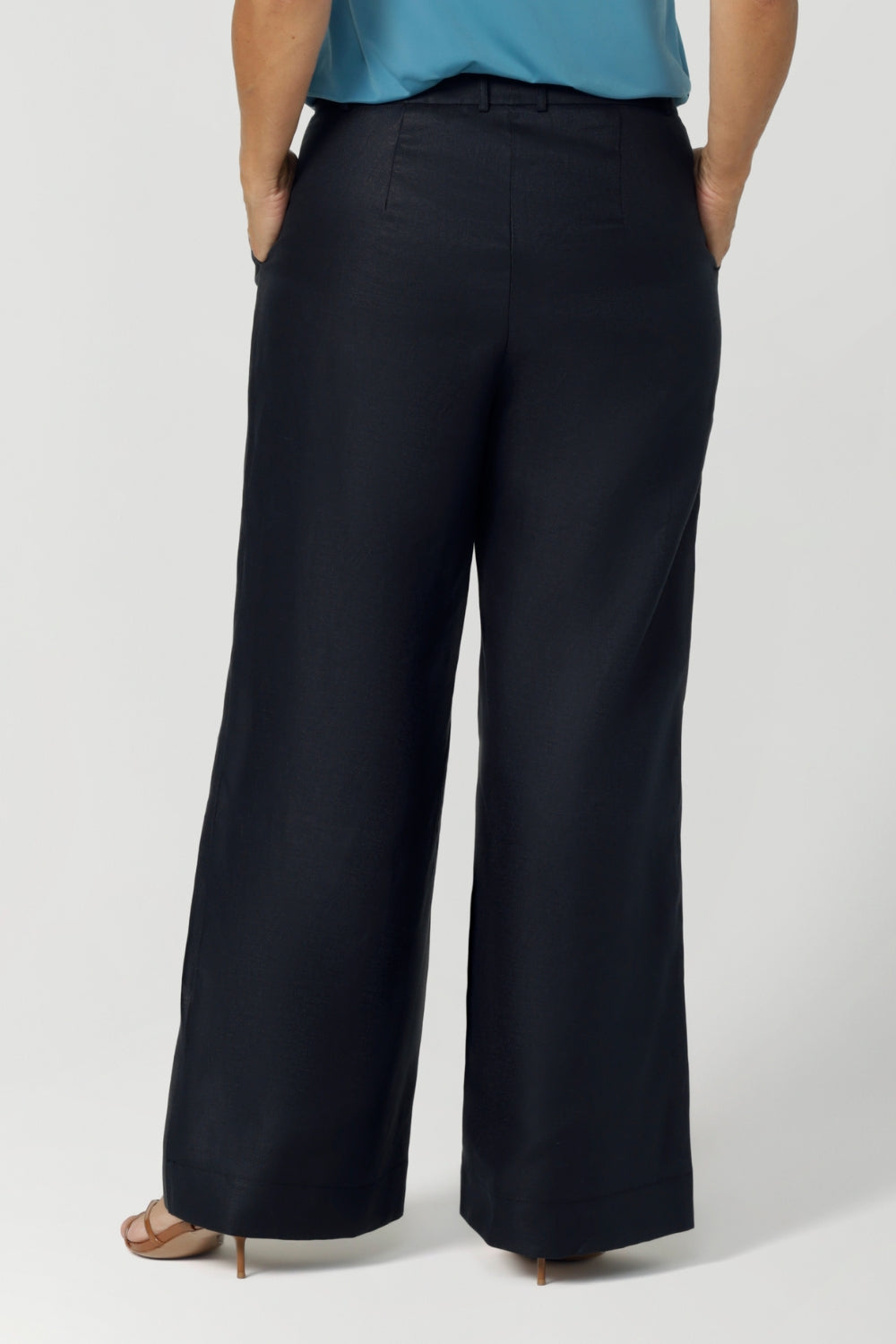 Back view of size 12 woman wears a tailored linen pant in 100% linen. Breathable linen fabrication in striking deep midnight navy colour. The perfect workwear pants with pockets that make great summer pants. Size inclusive fashion designed and made in Australia size 8 to 24. 