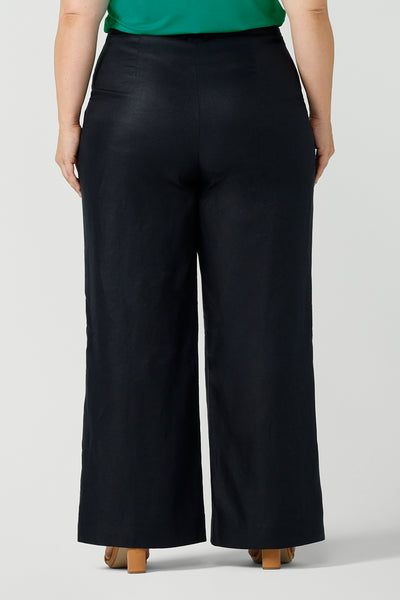 Back view size 18 curvy woman wears a tailored linen pant in 100% linen. Breathable linen fabrication in striking deep midnight navy colour. The perfect workwear pants with pockets that make great summer pants. Size inclusive fashion designed and made in Australia size 8 - 24. 