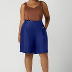Size 16 woman wears Cobalt Linen Bermuda short  in Cobalt. High waist short with pleat front and self cover buttons. Bermuda short length. Made in Australia for women size 8 - 24.