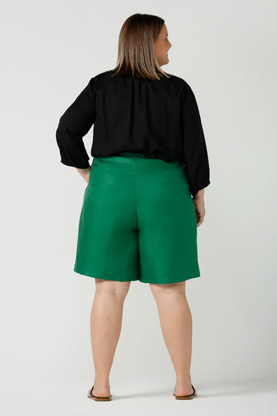 Back view of A curvy size 18 woman wears 100% Linen Bermuda shorts. The perfect smart casual shorts suitable for summer workwear to take you through to the weekend. Beautiful emerald green colour and soft tailoring details. Designed and made in Australia for sizes 8 -24.