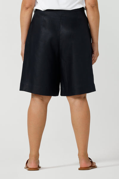 Back view of a curvy size 12 woman wears 100% Linen Bermuda shorts. The perfect smart casual shorts suitable for summer workwear to take you through to the weekend. Beautiful midnight navy colour and soft tailoring details. Designed and made in Australia for sizes 8 -24.