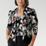 Crafted from a black dry-touch jersey fabric, the Moss Boss print showcases a subtle textured knit with embossed floral detailing in soft shades of white, grey, and coral. A center front seam and back yoke with a gentle tuck add tailored structure, while the curved shirt-tail hemline offers a flattering drape over the hips, whether worn loose or lightly tucked.