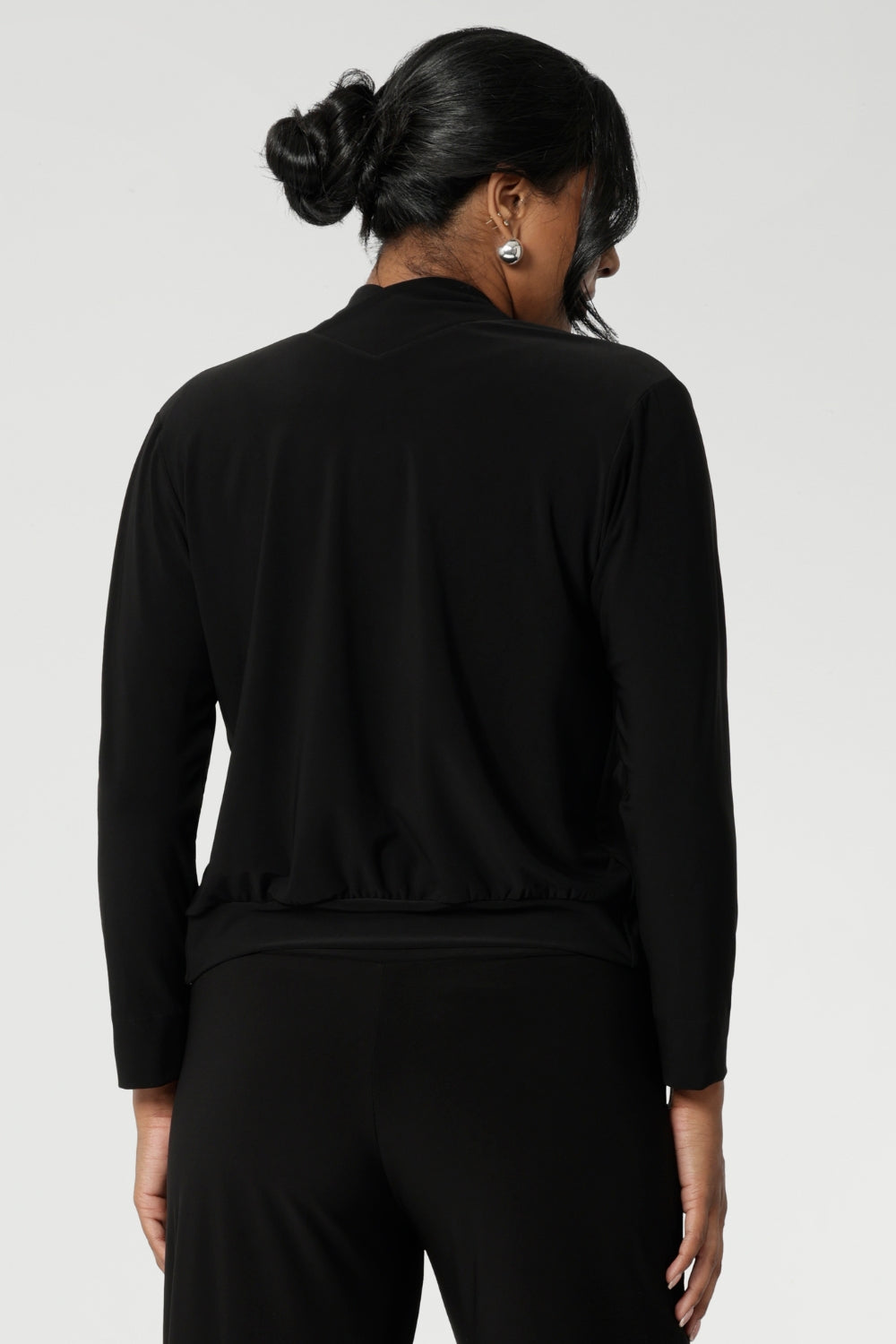 Back view image of size 10 woman, wearing black V-neck jacardi that features long sleeves, v neck & buttons. Designed to help women in Australia and New Zealand transition for the cooler months.. This jacket/cardigan is a transeasonal cover-up made from stretchy jersey fabric. Shop this jacket-cardigan hybrid in sizes 8-24.