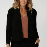 Over 40's woman wears a black V-neck jacardi with long sleeves. Designed to help women in Australia and New Zealand transition for cool weather. This jacket/cardigan is a transeasonal cover-up made from stretchy jersey fabric. Shop this jacket-cardigan hybrid in sizes 8-24.