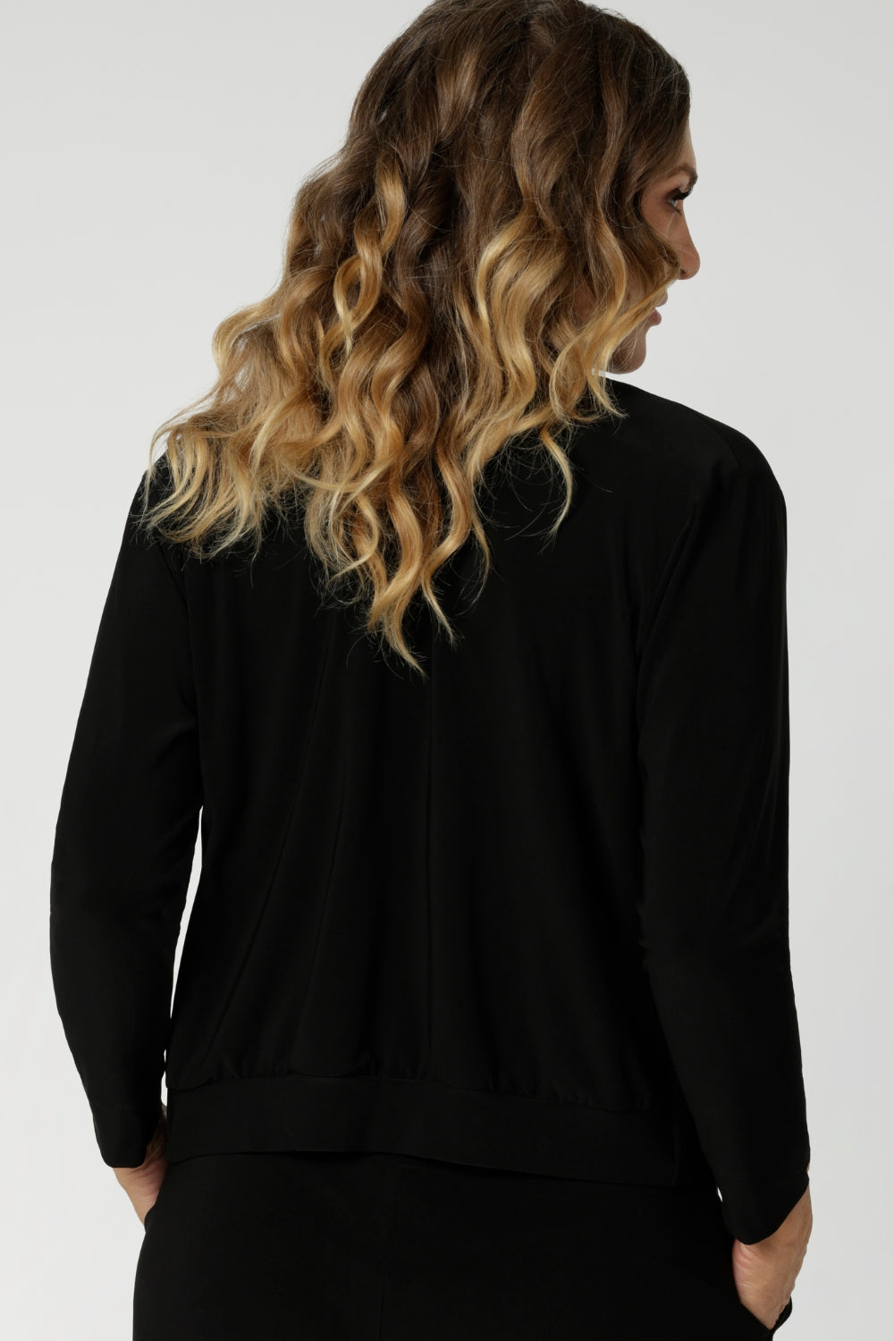 Back view image of size 12 woman, wearing black V-neck jacardi that features long sleeves, v neck & buttons. Designed to help women in Australia and New Zealand transition for the cooler months.. This jacket/cardigan is a transeasonal cover-up made from stretchy jersey fabric. Shop this jacket-cardigan hybrid in sizes 8-24.