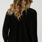 Back view image of size 12 woman, wearing black V-neck jacardi that features long sleeves, v neck & buttons. Designed to help women in Australia and New Zealand transition for the cooler months.. This jacket/cardigan is a transeasonal cover-up made from stretchy jersey fabric. Shop this jacket-cardigan hybrid in sizes 8-24.