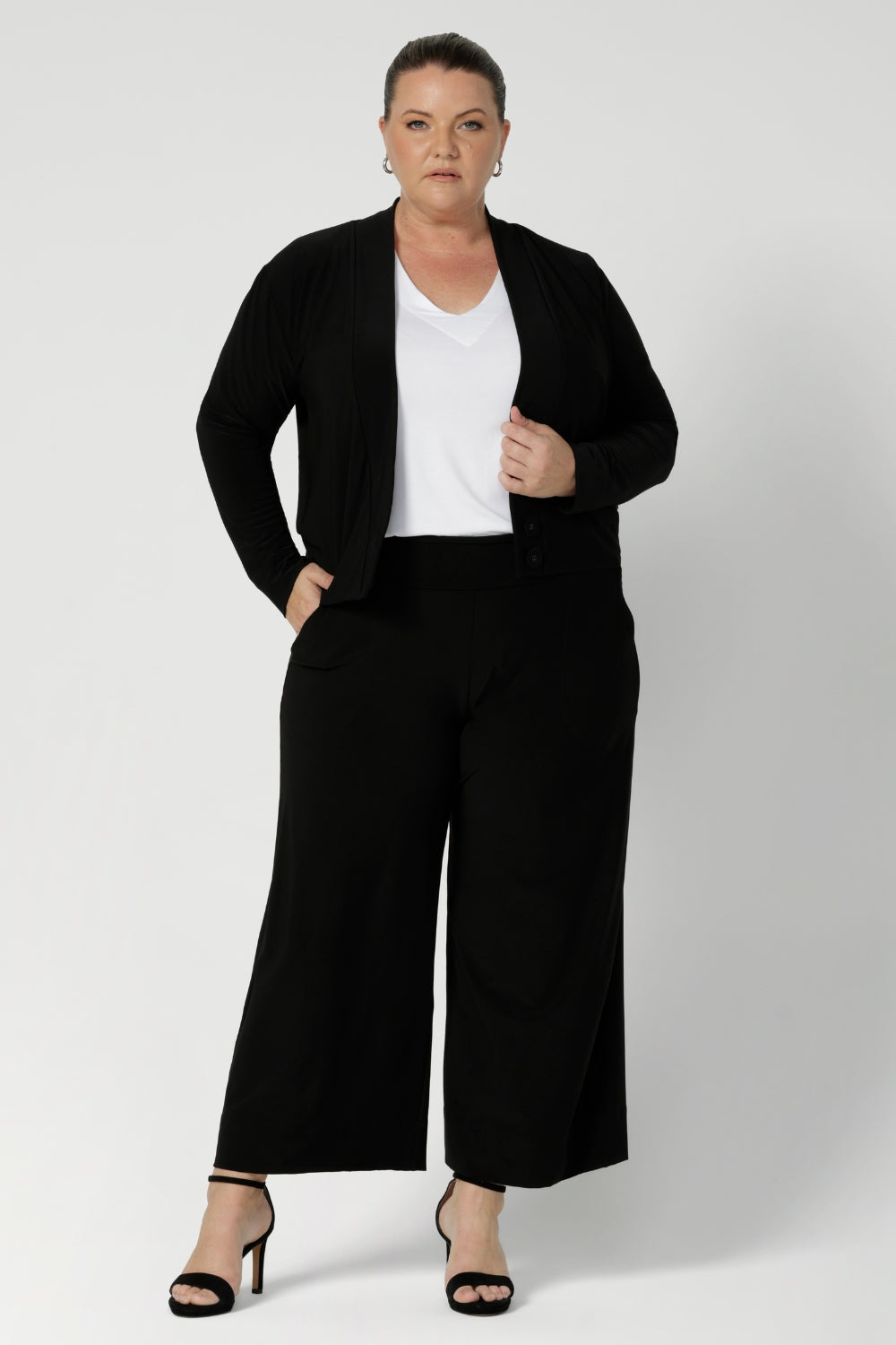 Size 18 woman wearing a black Jacardi - part jacket, part cardigan. This soft jacket is a transeasonal cover up. With V-neckline and long sleeves, this casual black jacket is made in stretch jersey for comfortable workwear layering. Available in sizes 8-24.