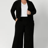 Size 18 woman wearing a black Jacardi - part jacket, part cardigan. This soft jacket is a transeasonal cover up. With V-neckline and long sleeves, this casual black jacket is made in stretch jersey for comfortable workwear layering. Available in sizes 8-24.