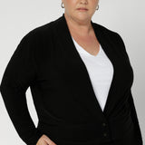 Size 18 woman wears black Jacardi, which is part jacket, part cardigan. This soft touch jacket is a transeasonal cover up. Featuring  V-neckline, long sleeves and front buttons. This casual black jacket is made from stretchy and comfortable jersey fabric. Easy care workwear jacket available in sizes 8-24.