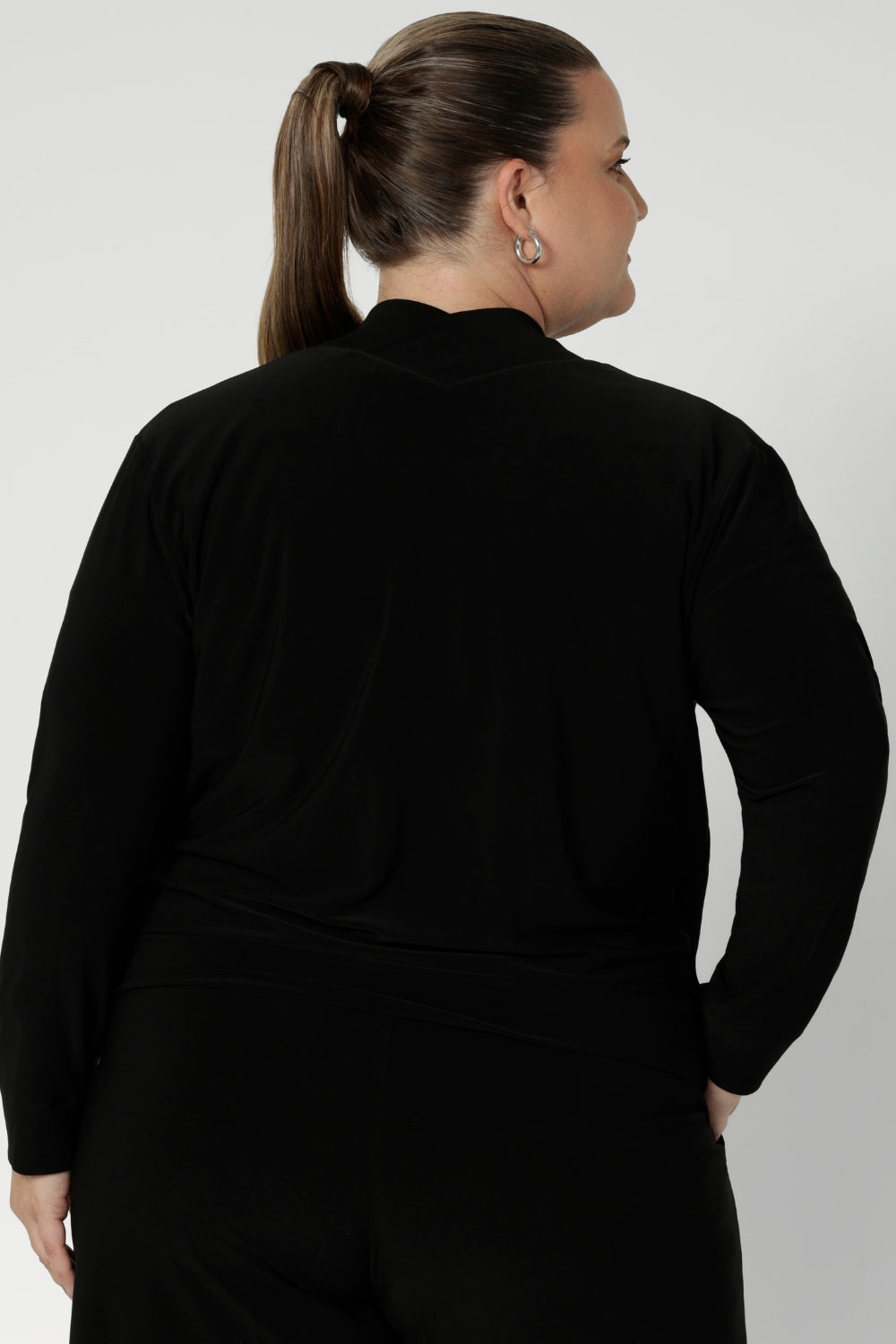 Back view of size 18 woman wears black, part jacket, part cardigan. Soft jacket is a transeasonal cover up, perfect for workwear layering. Featuring a V-neckline, long sleeves and buttons. This casual black jacket is made in stretch jersey for comfortability through the seasons. Available in sizes 8-24.