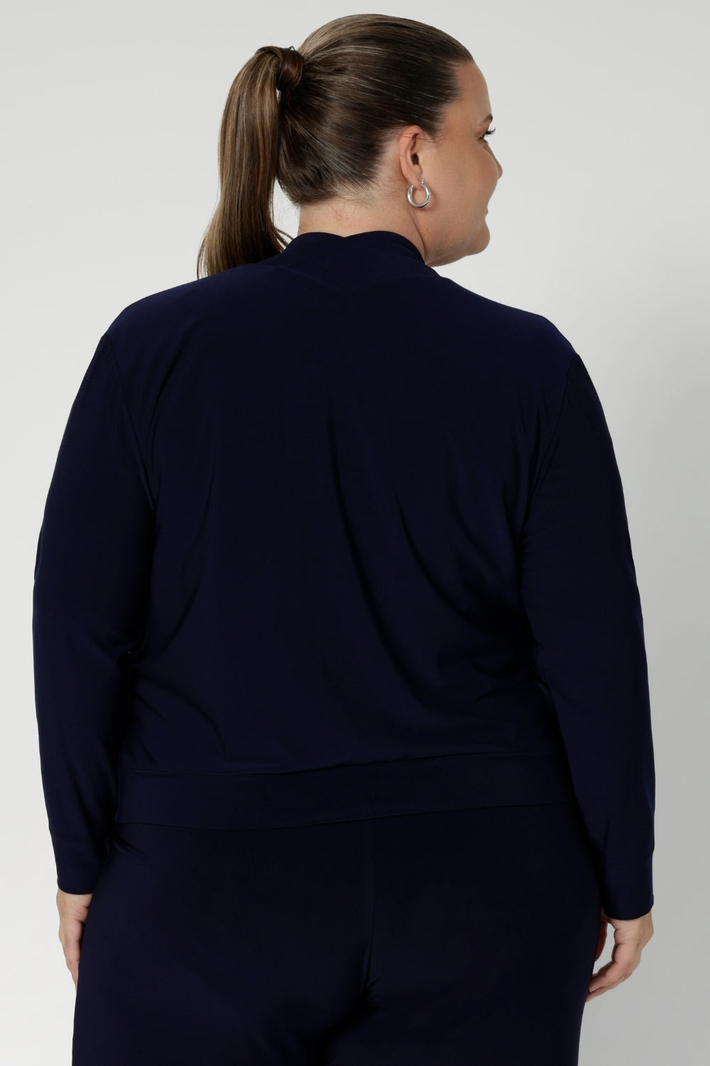 Size 18 woman wears a long sleeve jacket-cardigan hybrid in navy colour. Comfortable workwear jacket is made fro easing into the cooler months. Australian made from dry touch jersey fabric. Model wears Jacardi paired with white top and navy work pants to curate an easy back to work look.