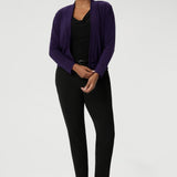 Whether you're dressing for a meeting or a day at the office, this stretchy, jacket-like cardigan combines versatility and elegance, offering a sophisticated layer for any professional setting. Size 10 woman wears her Purple Cardigan over a black top and matching pants outfit, for a subtle pop of colour.