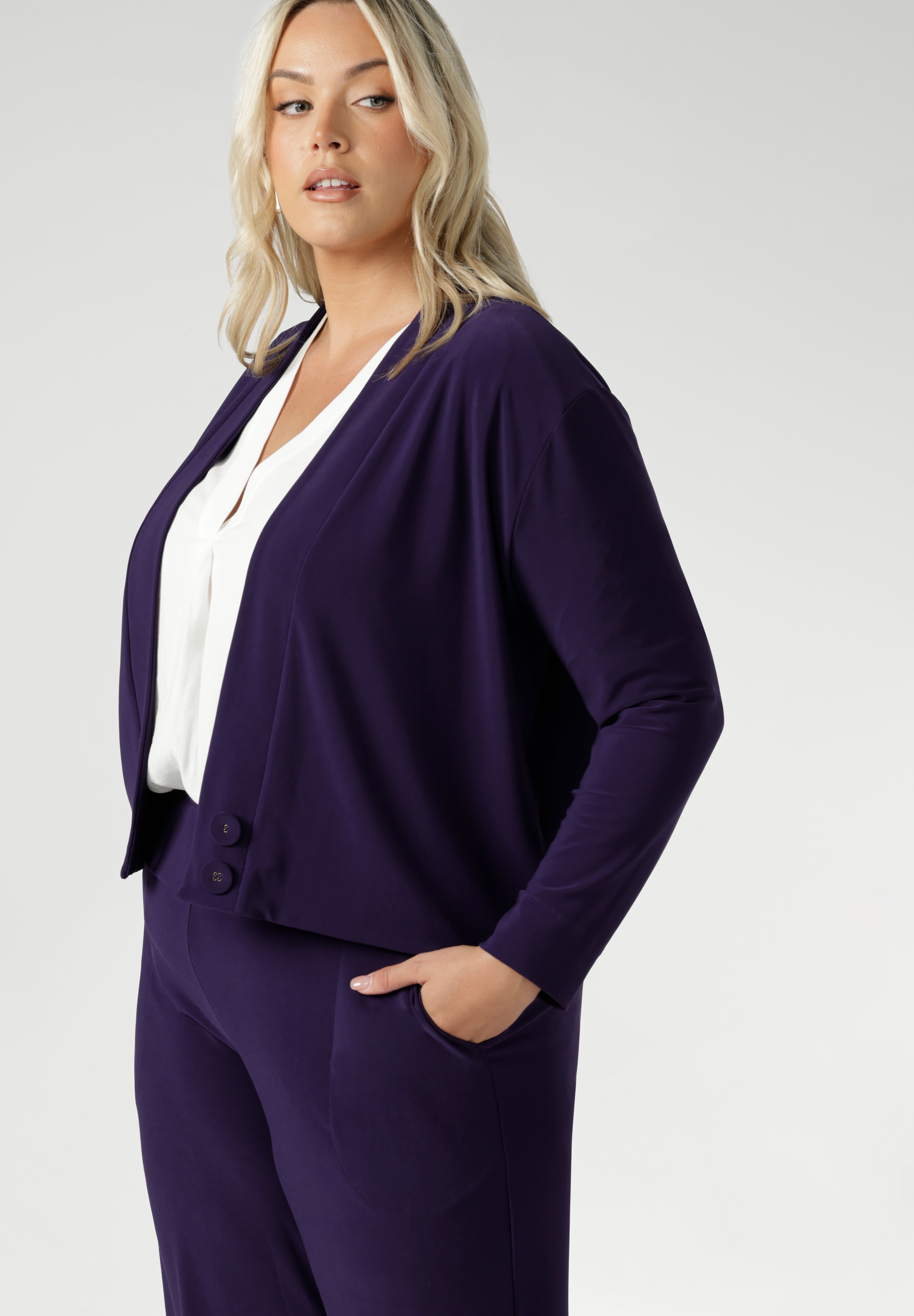 The Sandro Jacardi in Purple is crafted from a heavy-weight, dry-touch jersey base with a soft stretch that moves with you throughout the day, offering both comfort and a polished appearance. Plus size women wears purple cardigan with matching pull on workwear pants.