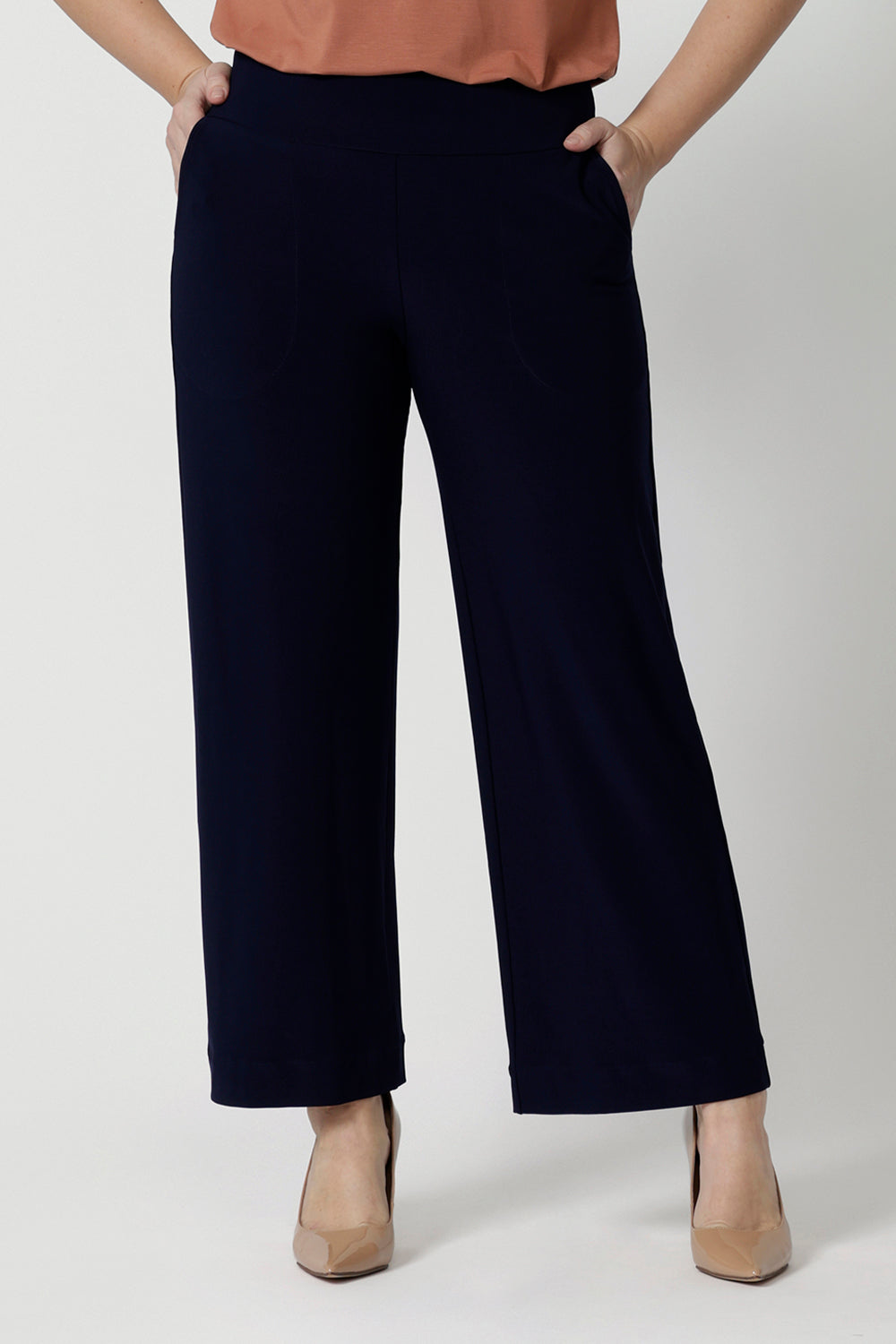 A petite height woman wears navy work pants in petite length with a jersey t-shirt in amber colour. Great pants for short women, these Australian-made pull-on trousers are available in sizes 8 to 24, petite to plus sizes.