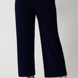 A petite height woman wears navy work pants in petite length with a jersey t-shirt in amber colour. Great pants for short women, these Australian-made pull-on trousers are available in sizes 8 to 24, petite to plus sizes.