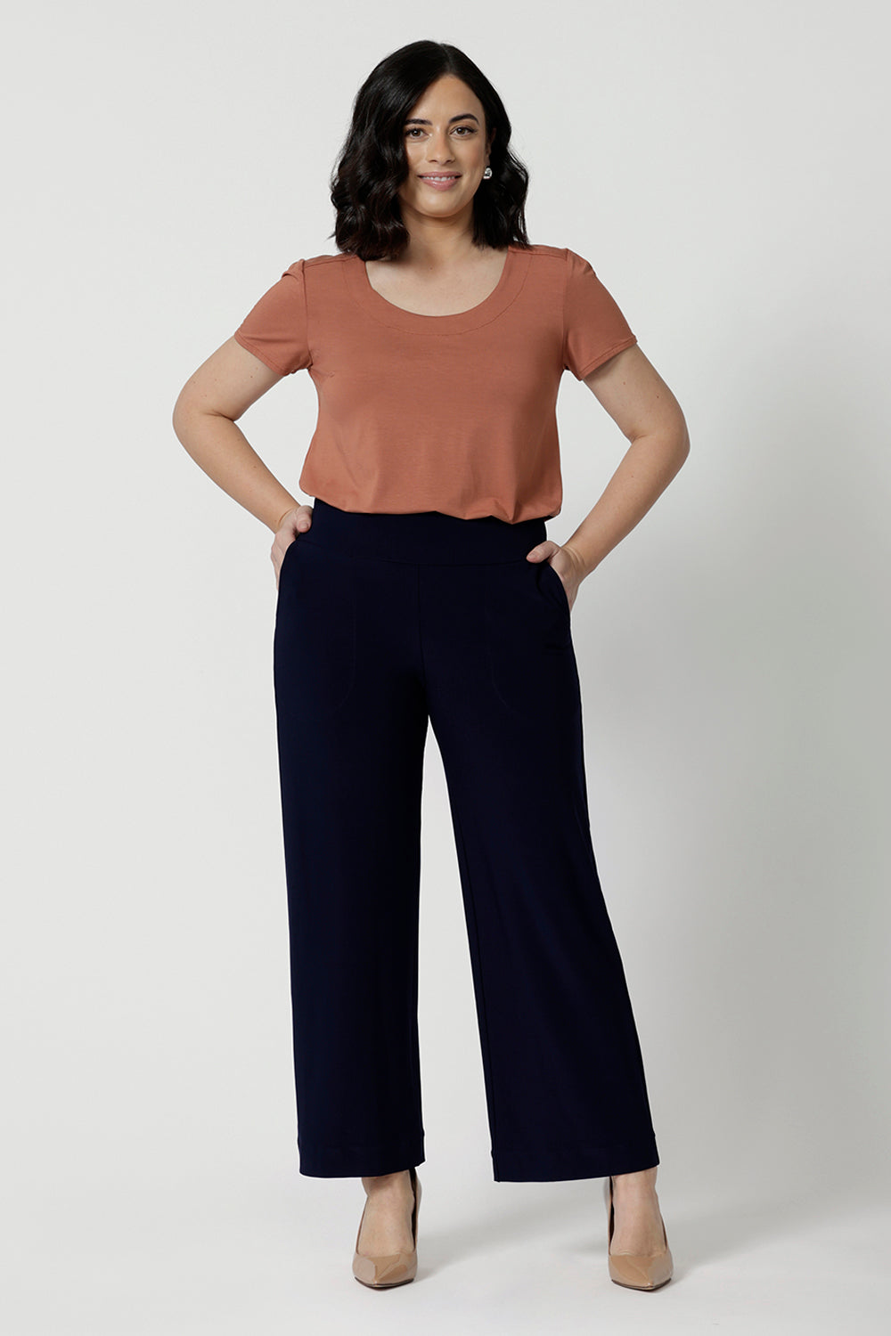 A petite height woman wears navy work pants in petite length with a jersey t-shirt in amber colour. Great pants for short women, these Australian-made pull-on trousers are available in sizes 8 to 24, petite to plus sizes.