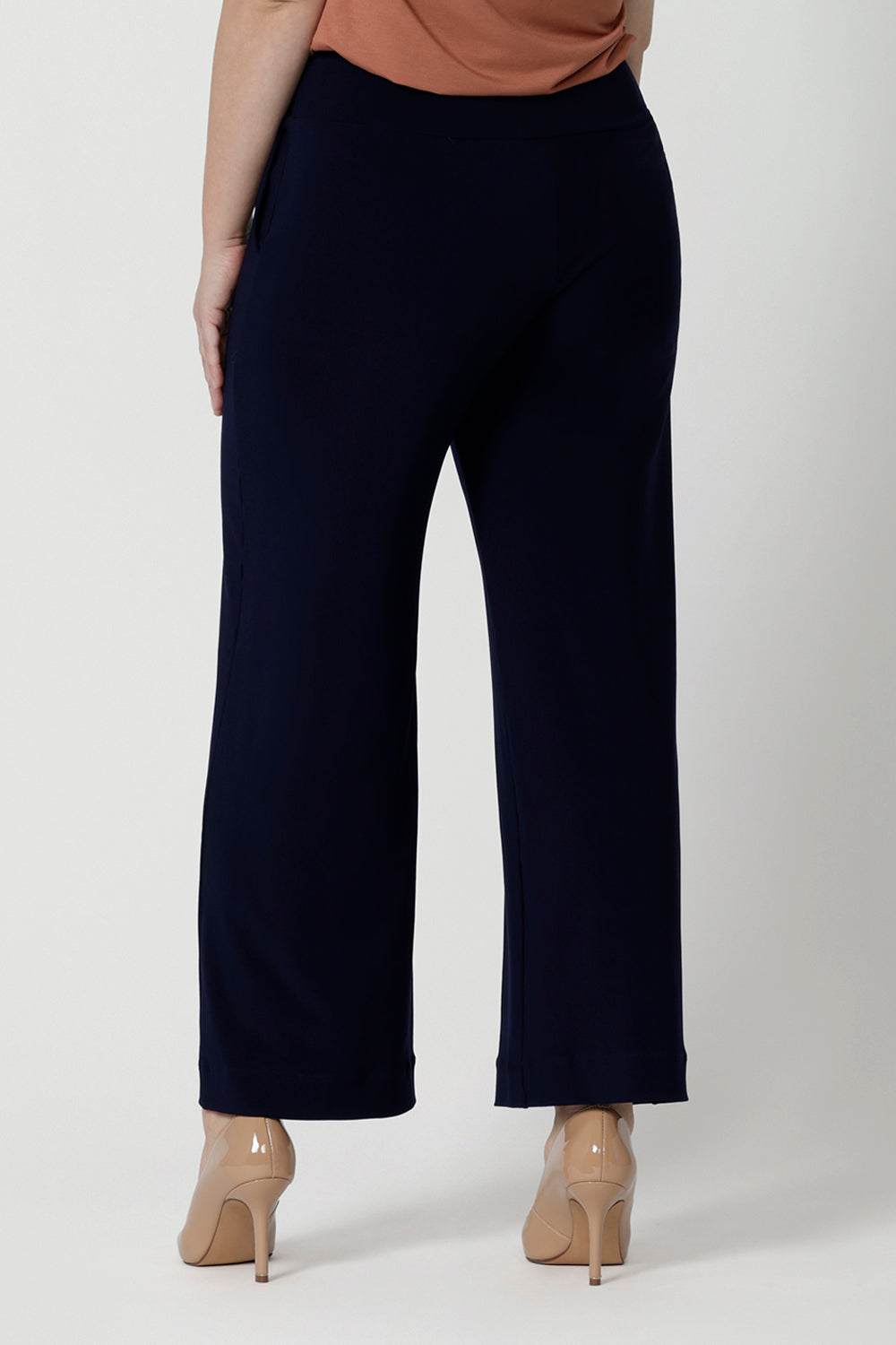 A petite height woman wears navy work pants in petite length with a jersey t-shirt in amber colour. Great pants for short women, these Australian-made pull-on trousers are available in sizes 8 to 24, petite to plus sizes.