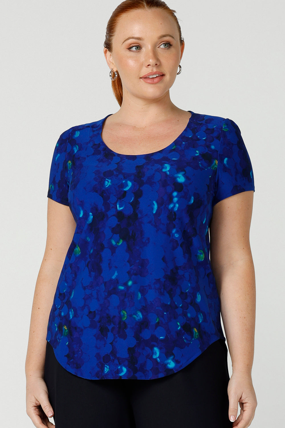 A curvy, size 12 woman wears a cobalt abstract jersey print, Round neck top with short sleeves. A good top for summer casual wear, or style tucked as a workwear top. Shop made in Australia tops in petite to plus sizes online at Australian fashion brand, Leina & Fleur.