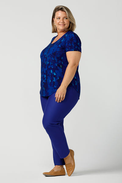A plus size, size 18 woman wearing a cobalt abstract jersey print, Round neck top with short sleeves styled with cobalt slim leg pants. A good top for summer casual wear, or style tucked as a workwear top. Shop made in Australia tops in petite to plus sizes online at Australian fashion brand, Leina & Fleur.