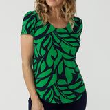 A size 10 woman wears the Sawyer Top in Green Jungle. A scoop neckline with a short sleeve. Soft jersey fabric for easy care. Styled back with Black Indi pants. Made in Australia for women size 8-24.