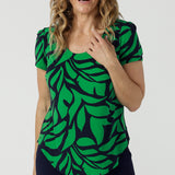 A size 10 woman wears the Sawyer Top in Green Jungle. A scoop neckline with a short sleeve. Soft jersey fabric for easy care. Styled back with Black Indi pants. Made in Australia for women size 8-24.