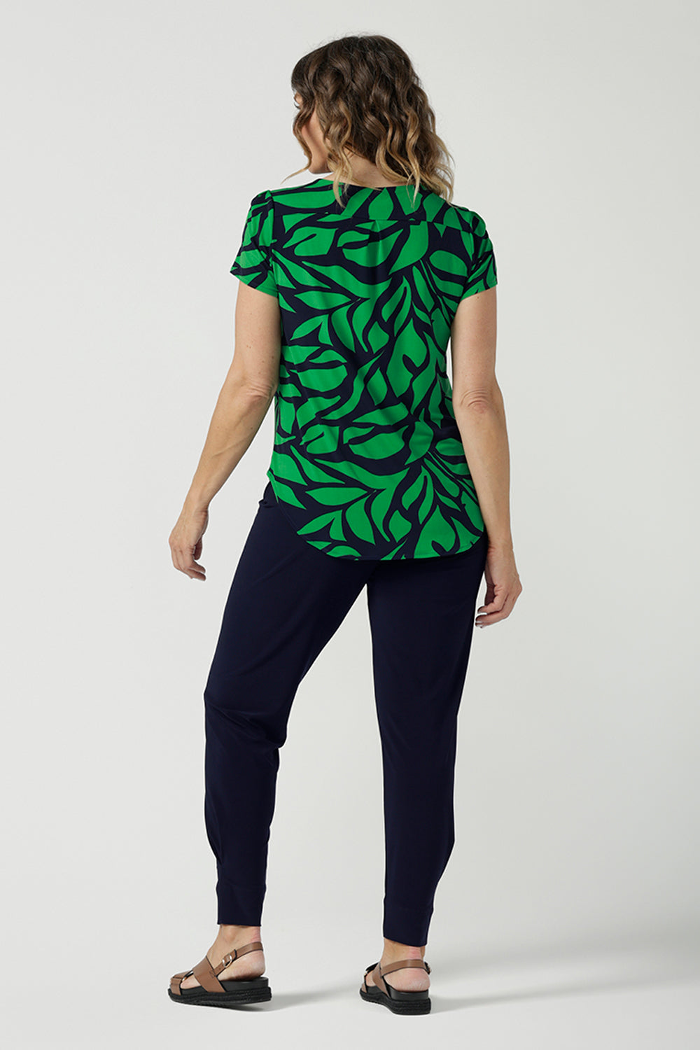 Back view of a size 10 woman wears the Sawyer Top in Green Jungle. A scoop neckline with a short sleeve. Soft jersey fabric for easy care. Styled back with Black Indi pants. Made in Australia for women size 8-24. Styled back with the Dutton Pant in Denim. 