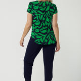 Back view of a size 10 woman wears the Sawyer Top in Green Jungle. A scoop neckline with a short sleeve. Soft jersey fabric for easy care. Styled back with Black Indi pants. Made in Australia for women size 8-24. Styled back with the Dutton Pant in Denim. 