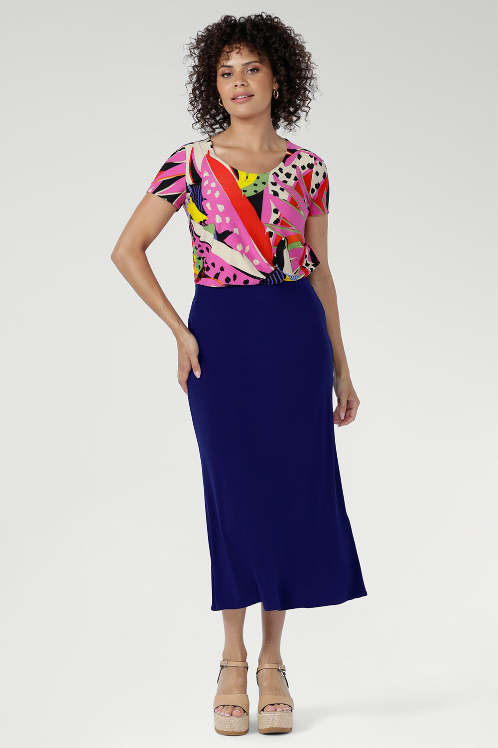 The Tucan print blends abstract strokes of pinks, reds, greens, and black on a warm cream base, creating a vibrant, artful pop that enlivens any outfit. Size 10 woman wears her Sawyer top with a cobalt colour skirt to make the print pop.