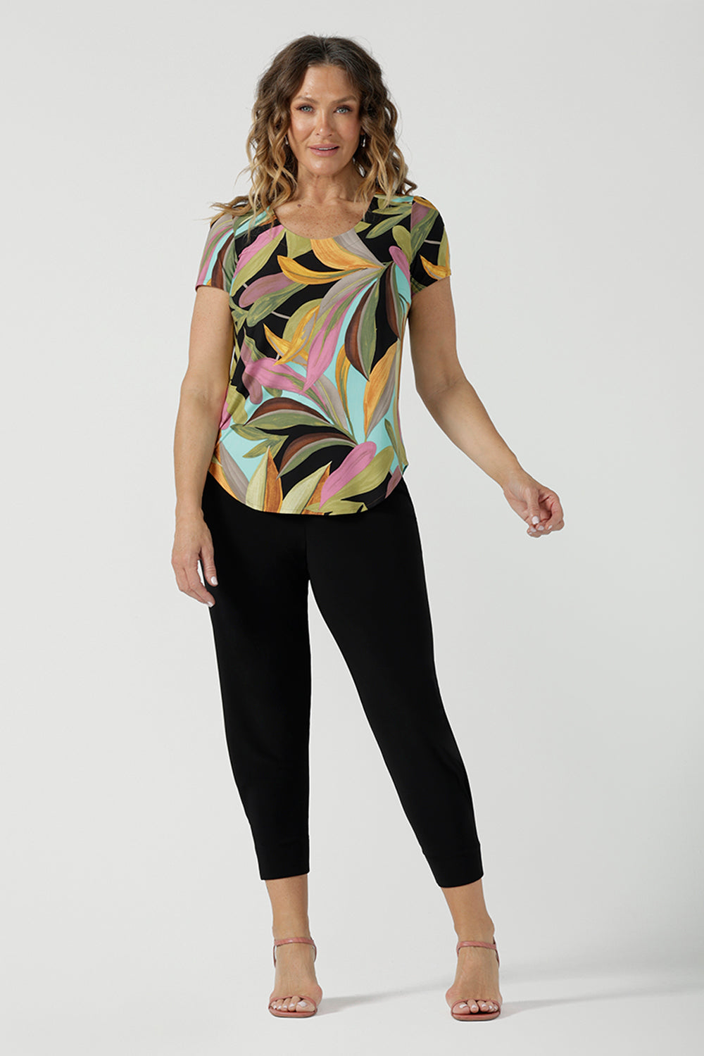 A size 10 woman wears the Sawyer Top in jersey with Zanzibar print. A multi coloured print with a black base and beautiful bright colours. Made in Australia for women size 8-24. Styled back with the Indi Pant in Black.  