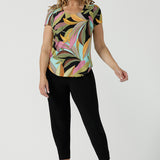 A size 10 woman wears the Sawyer Top in jersey with Zanzibar print. A multi coloured print with a black base and beautiful bright colours. Made in Australia for women size 8-24. Styled back with the Indi Pant in Black.  