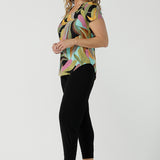 A size 10 woman wears the Sawyer Top in jersey with Zanzibar print. A multi coloured print with a black base and beautiful bright colours. Made in Australia for women size 8-24. Styled back with the Indi Pant in Black.  