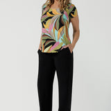 A size 10 woman wears the Sawyer Top in jersey with Zanzibar print. A multi coloured print with a black base and beautiful bright colours. Made in Australia for women size 8-24. Styled back with the Monroe Pant in Black.  