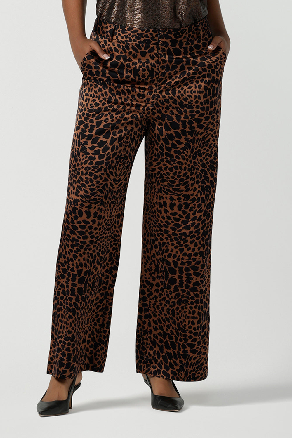 A woman wears the Sloane Pant in Bronze Animal. A satin straight leg waisted pant with pockets and a zip front. Made in high fashion Animal print fabric. Petite to plus size women size 8-24. Styled back with the Pele Shirt in Bronze animal.