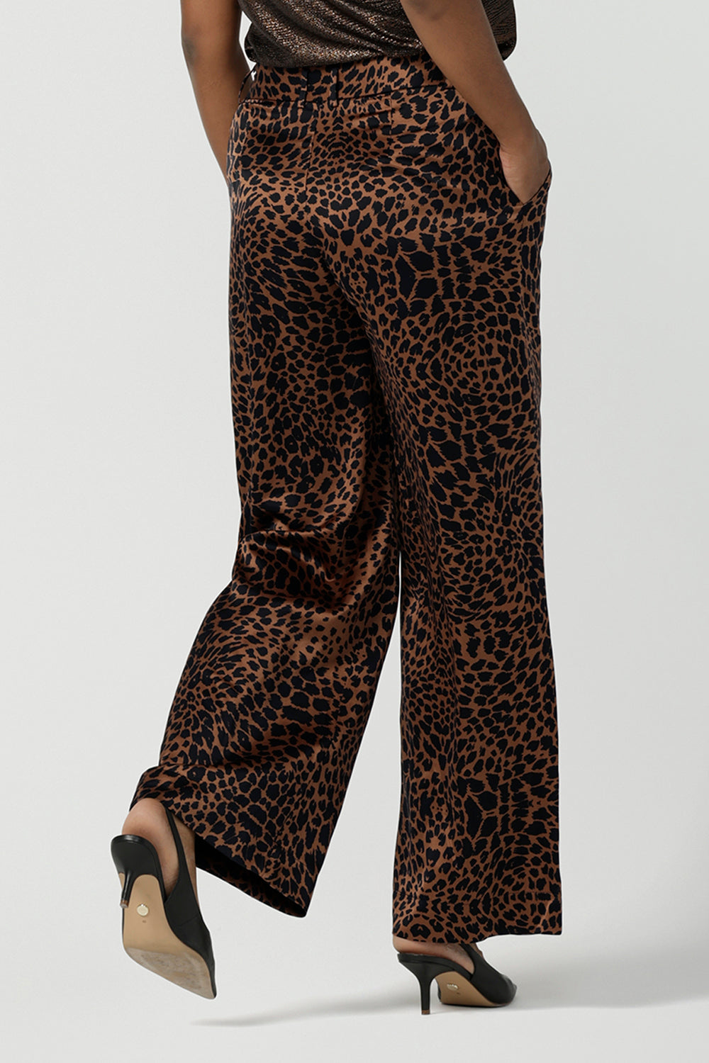 Back view of a woman wears the Sloane Pant in Bronze Animal. A satin straight leg waisted pant with pockets and a zip front. Made in high fashion Animal print fabric. Petite to plus size women size 8-24. Styled back with the Pele Shirt in Bronze animal.