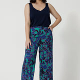 Full body shot image of a petite woman wearing wide leg printed pant and navy cami top. The abstract design of the set displays navy, pink and aqua blue colours. This Australian made shirt and pant set is made from satin rayon fabric that is breathable and comfortable. Leina and Fleur is a women’s clothing company that actively stocks plus sizes & petite sizes ranging from 8 to 24.