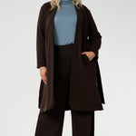 The Sorel Trench Coat is expertly tailored with a modern, sophisticated silhouette that elevates any wardrobe. Size 18 woman wears winter coat crafted from a luxurious winter-weight Modal fabric over wide length, blue turtle neck, and brown kitten heel.