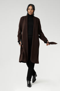 The Sorel Trench Coat is expertly tailored with a modern, sophisticated silhouette that elevates any wardrobe. Size 10 woman wears winter coat crafted from a luxurious winter-weight Modal fabric over long length black pants, black turtle neck, and high heel boots for an elevated workwear look. 
