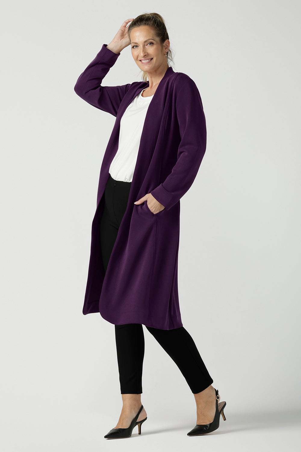 A size 10 woman wears the Sorel Trenchcoat in Amethyst. Inner seam pockets with, long sleeves with wrap tie. Made in Australia using soft modal scuba material. Made in Australia for women size 8 - 24.