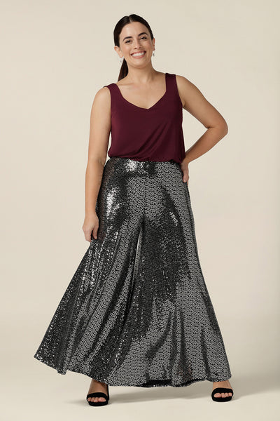 A woman wears sparkly sequin pants for cocktail and evening wear. In size 10, these wide leg cocktail wear trousers are great sequin pants for dazzling occasionwear style! Worn with a plum red cami top, these wide leg sequin occasionwear pants are available to shop in petite to plus sizes at Leina & Fleur.